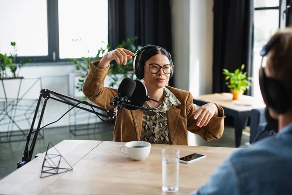 Asiático Rádio Host Óculos Fones Ouvido Gesticulando Perto Confuso Colega — Fotografia de Stock