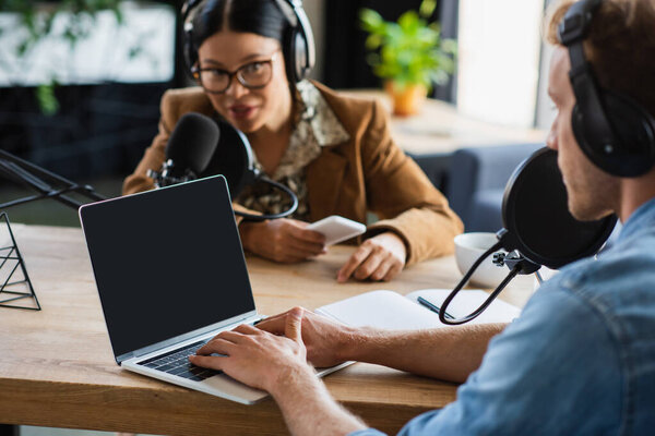 размытый радиохост с помощью ноутбука рядом с азиатским коллегой записи подкаста в студии 