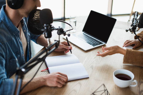обрезанный вид радиоведущего, указывающего на ноутбук рядом с коллегой в студии 