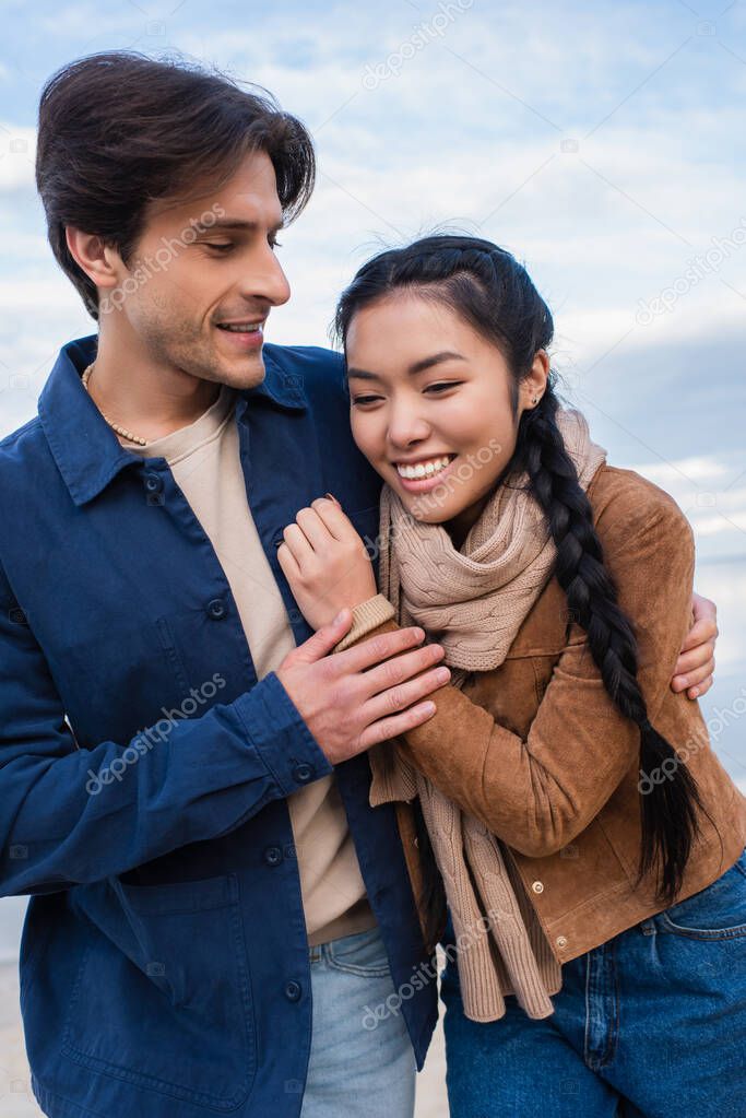 Positive multiethnic couple hugging outdoors during weekend 