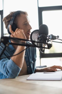 Radyo sunucusunun yan görüntüsü kulaklıkları ayarlıyor ve podcast yaparken konuşuyor 