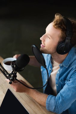 Podcast stüdyosunda elinde kahve fincanı tutan pozitif radyo sunucusunun yüksek açılı görüntüsü 