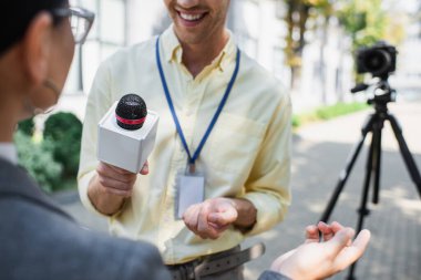 cheerful reporter holding microphone near blurred businesswoman gesturing while giving interview  clipart