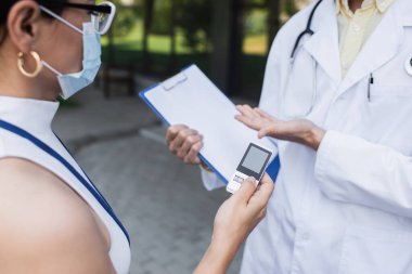 Maskeli Asyalı muhabir elinde ses kaydedici ile beyaz önlüklü doktorun yanında. 