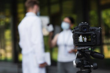 Ekranda tıbbi maskeli doktorun yanında mikrofon tutan Asyalı gazeteciyle dijital kamera
