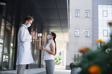 Asyalı gazetecinin mikrofonlu yan görüntüsü klinik yakınlarındaki doktorla röportaj yapıyor.