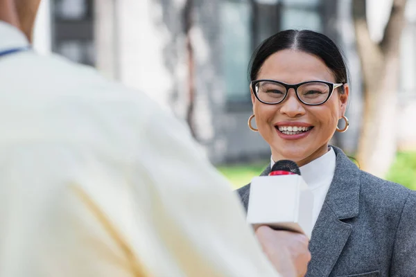 Blurred Reporter Standing Microphone Positive Asian Businesswoman Glasses — Stock Photo, Image