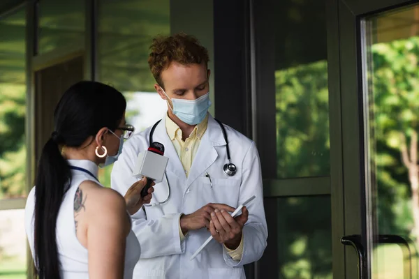 Médico Máscara Médica Apontando Para Tablet Digital Perto Jornalista Tatuado — Fotografia de Stock