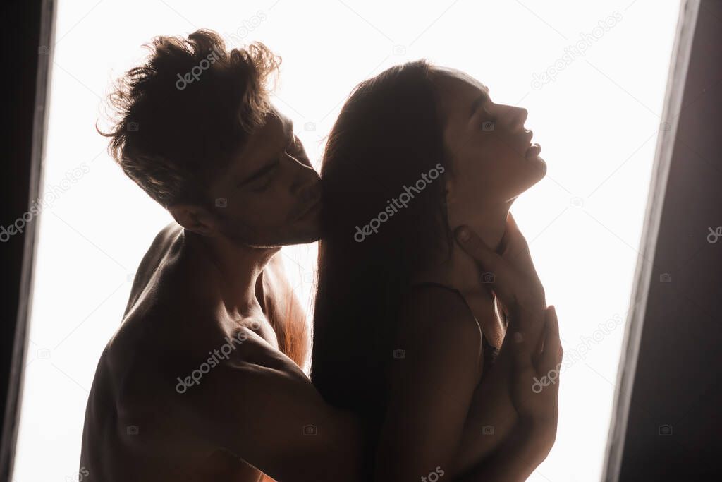 Shirtless man touching neck of passionate girlfriend near lamp on black background