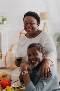 Şükran Günü yemeğinin yanında şarap kucaklayan kocası olan Afro-Amerikalı bir kadın. 
