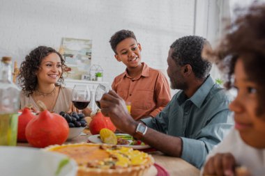 Gülümseyen Afrikalı Amerikalı çocuk Şükran Günü yemeğinde büyükbabasıyla konuşuyor.