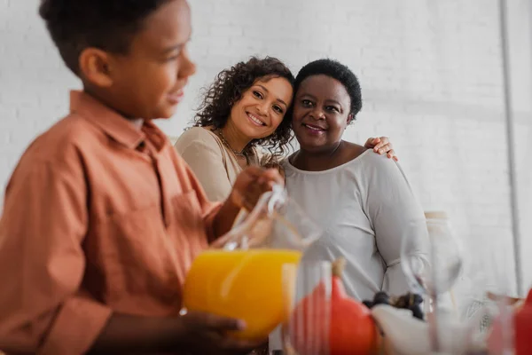 Glimlachende Afro Amerikaanse Vrouwen Kijken Naar Wazig Kind Met Sinaasappelsap — Stockfoto