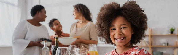 Sonriente Chica Afroamericana Mirando Cámara Cerca Familia Borrosa Cena Acción —  Fotos de Stock