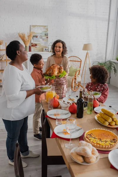 Mujer Afroamericana Sonriente Sosteniendo Pavo Cerca Familia Cena Acción Gracias — Foto de Stock