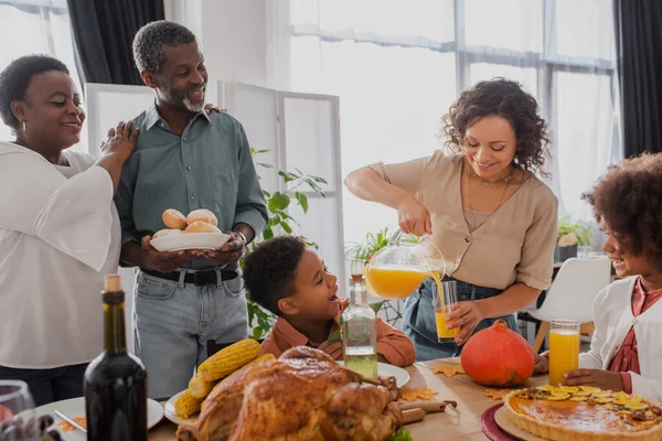 Sonriente Mujer Afroamericana Vertiendo Jugo Naranja Cerca Familia Cena Acción — Foto de Stock