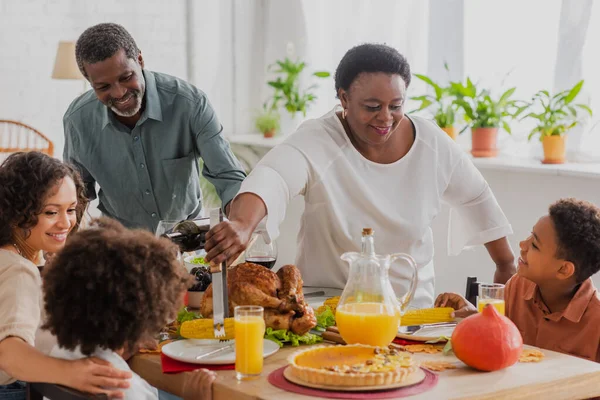 African american woman putting food on plates near family during thanksgiving dinner