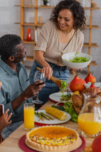 Mujer Afroamericana Sonriente Sirviendo Ensalada Cerca Padre Con Celebración Vino — Foto de Stock