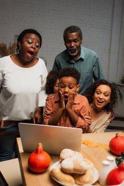 Şaşırmış Afrikalı Amerikalı çocuk laptopun ve ailenin yanında yüzüne dokunuyor.