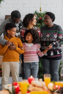 Gülümseyen Afro-Amerikan ailesi evde Noel kutlaması sırasında el ele tutuşuyorlar.