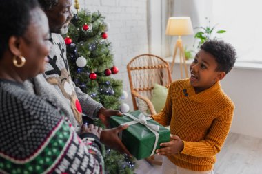 Şaşırmış Afrikalı Amerikalı çocuk bulanık büyükanne ve büyükbabasından Noel hediyesi alıyor.