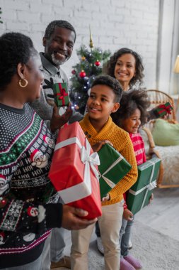 Afro-Amerikan ailesi evde Noel hediyeleri tutarken gülümsüyor.