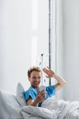 Hastanedeki akıllı telefondan görüntülü arama yapılırken mutlu hasta el sallıyor. 