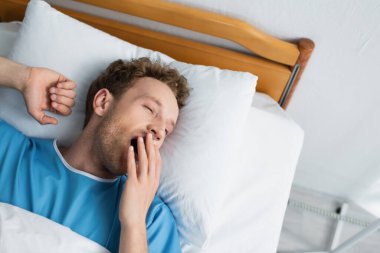 top view of patient yawning while lying in hospital bed clipart