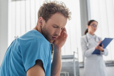 Hastanedeki bulanık bir doktorun yanında baş ağrısı çeken kıvırcık bir hasta. 