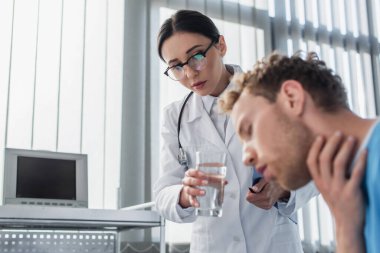 Gözlüklü doktor hastanedeki hasta hastaya bir bardak su veriyor. 