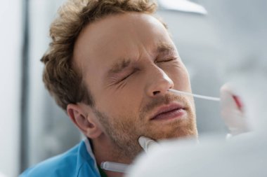 Burnu kapalı kıvırcık bir hastanın burnundan örnek alıp nazal PCR testi yapan lateks eldivenli bir doktor.