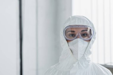 Kişisel koruyucu ekipman ve gözlüklü doktor kameraya bakıyor.