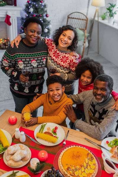 クリスマスディナーの間にカメラを見るアフリカ系アメリカ人の家族の喜びの角度の高い眺め — ストック写真