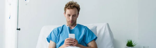 Paciente Rizado Usando Teléfono Inteligente Mientras Descansa Cama Del Hospital —  Fotos de Stock