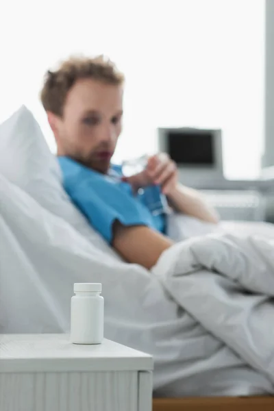 Flaska Med Läkemedel Nattduksbordet Nära Suddig Patient Sjukhussäng — Stockfoto