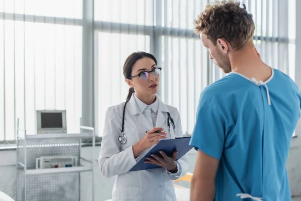 Brünette Ärztin Mit Klemmbrett Schaut Lockige Patientin Krankenhaus — Stockfoto