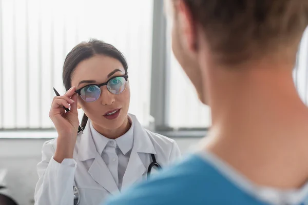 ブルネット医師ともにペン調整眼鏡をかけながら見ている間にぼやけた患者で病院 — ストック写真