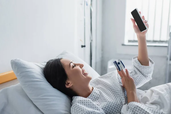 Wanita Bahagia Dengan Oksimeter Jari Menggunakan Smartphone Saat Berbaring Tempat — Stok Foto