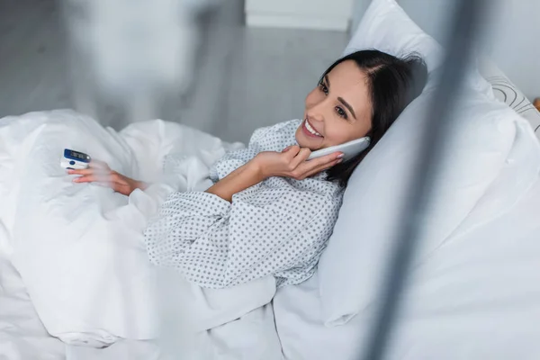 Mulher Sorridente Com Oxímetro Dedo Falando Smartphone Enquanto Deitado Cama — Fotografia de Stock