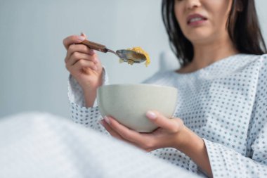 cropped view of disgusted patient holding spoon with corn flakes and bowl in hospital  clipart