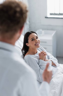 Hasta önlüklü neşeli kadın beyaz önlüklü bulanık doktora bakıyor. 