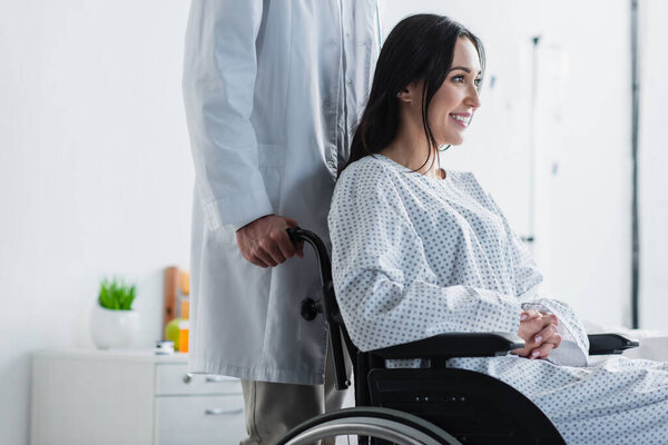 doctor in white coat standing behind smiling disabled woman in wheelchair 