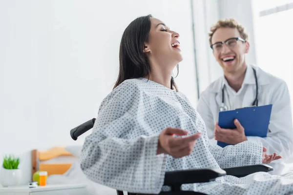坐在轮椅上的快乐女人在朦胧的医生身边笑着 — 图库照片