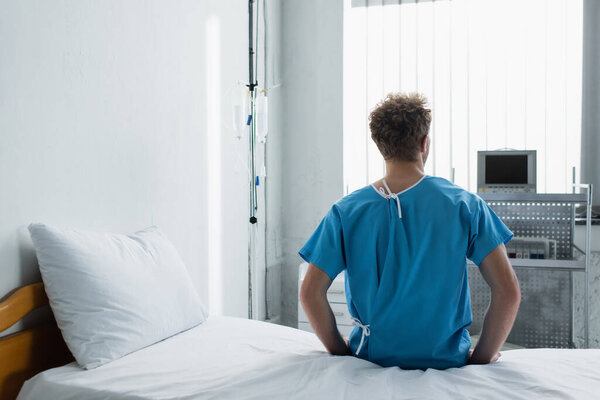 back view of curly man sitting on hospital bed 