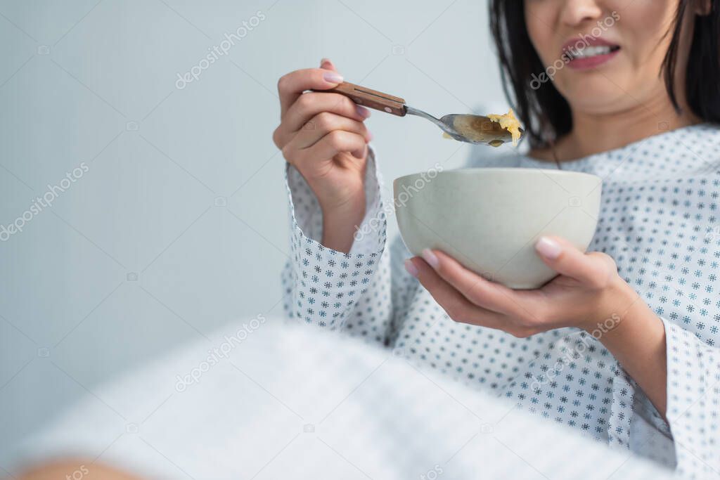 Cropped view of disgusted woman holding spoon with corn flakes and bowl in hospital