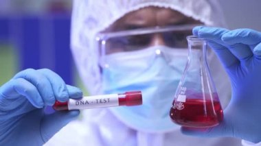 Bulanık Hintli bilim adamı laboratuarda DNA testi ile matara ve test tüpü tutuyor.