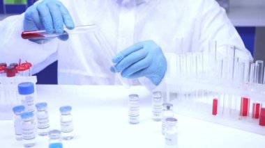 Laboratuvardaki aşıların yanında test tüpüne kan döken bilim adamının kırpılmış görüntüsü. 