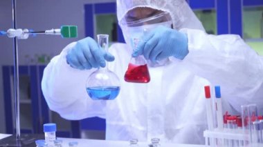 Hintli bilim adamı mataralarda numune sallıyor ve laboratuvarda pano alıyor. 