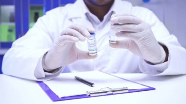 Bilim adamının elinde aşı dolu kavanozlarla laboratuvarda pano başında görüntüsü. 