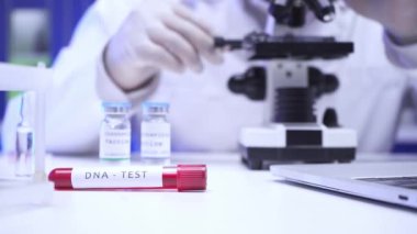 Laboratuvarda bilim adamı ve dizüstü bilgisayarın yanında DNA harfleri bulunan test tüpü görüntüsü. 