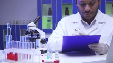 Hintli bilim adamı mikroskop ve laboratuardaki test tüplerinin yanında panoya yazı yazıyor. 